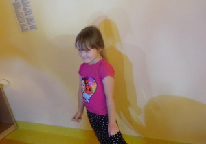 Uśmiechnięta dziewczynka stoi pod ścianą.
